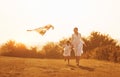 Daughter with her mother have fun together by running with kite on the field. Illuminated by beautiful sunlight