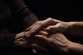 The daughter is holding the hand of her mother elderly in dark background Royalty Free Stock Photo