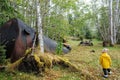 A daughter and mother exploring an abandoned settlement, including an old car and oil drum, surrounded by forest Royalty Free Stock Photo