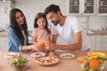 Daughter, mother and father clicking glasses with orange juice together standing at kitchen table