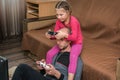 Daughter sits on DadÃ¢â¬â¢s shoulders and plays video games using gamepads at home. A man and a child hold game joysticks in their