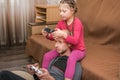 Daughter sits on DadÃ¢â¬â¢s shoulders and plays video games using gamepads at home. A man and a child hold game joysticks in their