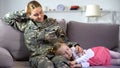 Daughter sleeping on american soldier mothers knees, resting on sofa at home