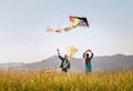 Daughter with smiling father while they flying a colorful kites on the high grass meadow in the mountain fields. Warm family