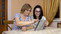 Daughter teaches mother how to use a tablet. A young woman shows her old mother where to click on a tablet. The family Royalty Free Stock Photo