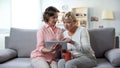 Daughter teaching mother how to use banking app, sitting on sofa with tea cup