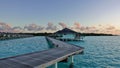 Dawn in the Maldives. A wooden walkway runs over the aquamarine ocean