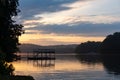 Dawn over Lake Lanier; silhouette of a dock and trees on a lake under a purple and orange sky with clouds Royalty Free Stock Photo