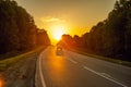 Dawn over the road leading to the morning forest with a passing car