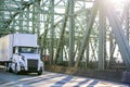 Day cab big rig white semi truck with roof spoiler transporting goods in dry van semi trailer running on the truss Columbia River Royalty Free Stock Photo