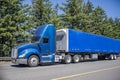 Day cab blue big rig semi truck with roof spoiler transporting cargo in blue dry van semi trailer running on the highway road Royalty Free Stock Photo