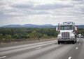 Clean day cab powerful big rig white semi truck transporting industrial cargo on flat bed semi trailer running on the wide one way Royalty Free Stock Photo