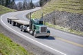 Day cab classic green big rig semi truck tractor transporting two empty flat bed semi trailers driving on the winding mountain Royalty Free Stock Photo