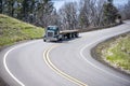 Day cab dark green classic big rig semi truck with two empty flat bed semi trailers running on the winding mountain road at Royalty Free Stock Photo