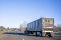 Day cab red big rig semi truck transporting commercial cargo in black covered semi trailer running on the straight wide highway