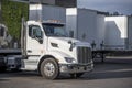 Day cab white big rig semi truck with dry van semi trailer standing on the warehouse parking lot in row with another semi trailers Royalty Free Stock Photo