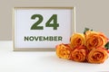 Day of the month 24 November calendar photo frame and yellow rose on a white table