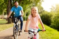 Day in the park. Happy family of caucasian father and girl riding bicycles outdoors in the summer, smiling at camera Royalty Free Stock Photo