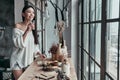 Day starts with healthy breakfast. Attractive young woman drinking water with lemon and smiling while standing near the window Royalty Free Stock Photo