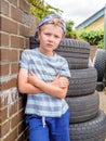 Day view cute little child boy posing next to stack of used tyres over brick english wall Royalty Free Stock Photo