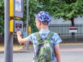 Day view little child boy with backpack pressing pedestrian signal button to cross the British road