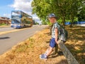 Day view little child boy traveller with backpack sitting next to UK road