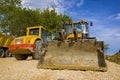 Yellow excavator with a shovel and single drum roller at the construction site