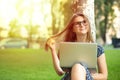 Daydreaming about future. Pensive woman teenage girl female with a laptop sitting near a tree on a green grass lawn isolated city Royalty Free Stock Photo
