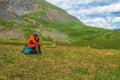 Daydreaming while sitting in nature. Rest time on a hike, a rest stop. Tired hiker man sits on a large backpack and happily looks