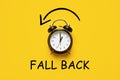 Daylight saving day. Fall Back. Black Alarm clock and autumn leaves and text Fall Back on yellow background. Daylight