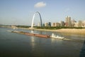 Daytime view of tug boat pushing barge down Mississippi River in front of Gateway Arch and skyline of St. Louis, Missouri as seen