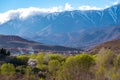 Daytime wide angle shot of Beautiful landscape of snow capped mountains and bushes and a village in the valley. Atlas, Morocco
