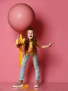Dazed young lady, teen girl in jeans and yellow t-shirt with glass of yellow juice stands at big pink balloon with yellow tape Royalty Free Stock Photo