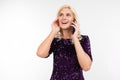 Dazzling blonde business woman in purple shiny dress discussing business on the phone on a white background with copy