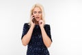 Dazzling blonde girl in a blue shiny dress chatting on the phone on a white background with copy space