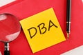 DBA the inscription on the sticker lying on a red notebook next to a magnifying glass and a fountain pen