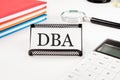 DBA text on a business card next to office supplies on a white background