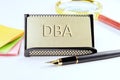 DBA text on a gold plastic card with convex text next to office supplies on a white background