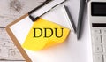 DDU word on yellow sticky with calculator, pen and clipboard Royalty Free Stock Photo