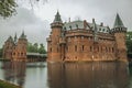 De Haar Castle facade with ornate brick towers and water moat on rainy day, near Utrecht.