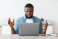 Deadline Stress. Annoyed black man sitting at workplace looking at laptop screen