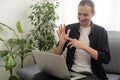 Deaf or hard hearing happy smiling young caucasian man uses sign language while video call using laptop while sitting on