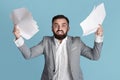 Dealing with workplace stress. Angry overworked office employee grasping paper documents over blue background