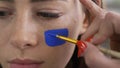 Deatailed face of a young beautiful woman. Artist painting blue icon on the girl`s face using small soft brush. Body art