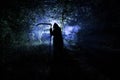 Death with a scythe in the dark misty forest. Woman horror ghost holding reaper in forest