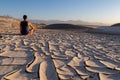 Death Valley - Man sitting on dry cracked clay crust at Mesquite Flat Sand Dunes in Death Valley National Park, California, USA