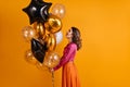 Debonair girl looking at party balloons. Indoor photo of pleased woman in pink blouse isolated on orange background