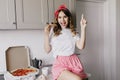 Debonair woman in romantic pajama eating pizza. Enchanting female model posing in kitchen with cup