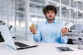 Debt, bankruptcy, foreclosure, fraud. A young Latin American businessman is sitting in the office at the table, holding Royalty Free Stock Photo