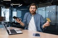 Debt, bankruptcy, foreclosure, fraud. A young man is sitting in the office at the table, holding a phone and a credit Royalty Free Stock Photo